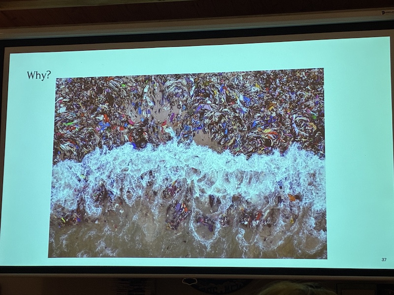A top-down view of a beach, where the tide is soaking an existing widespread deposit of abandoned clothes washed in from the ocean.