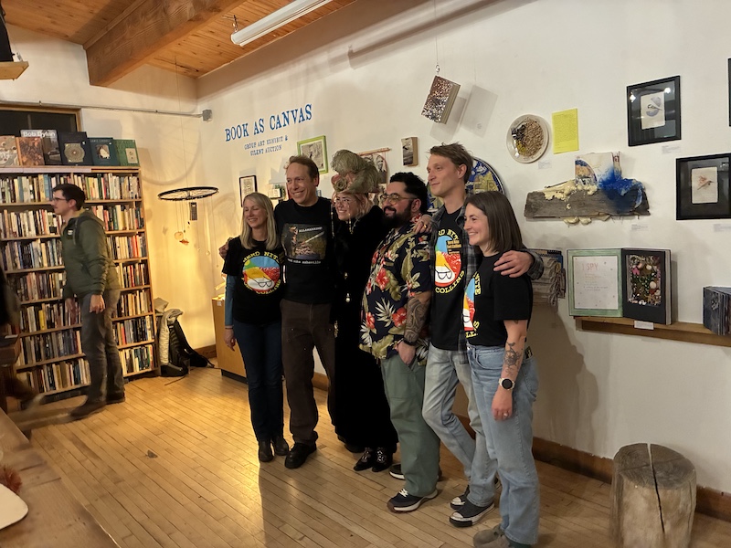 Six individuals stand together for a photo, captured from one side while they look ahead. Andres is wearing a floral shirt, fourth from the left. Andres and Chris occupy the center of the lineup, with four event organizers distributed on either side.