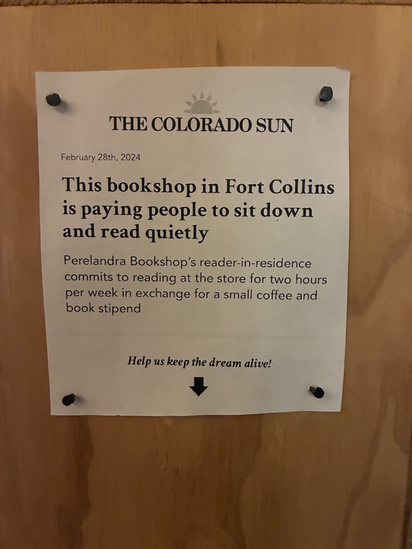 A sign posted inside, wearing the names Colorado Sun (a local state news operation, and Perelandra Bookshop. The sign indicates that interested parties can take a dangling strip to read for two hours per week at the venue and be compensated with coffee and a book stipend.