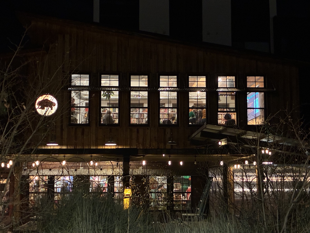After dark, a two-story exterior is viewed at its long side. In the second floor, several windows show the illumination of the meeting taking place inside.
